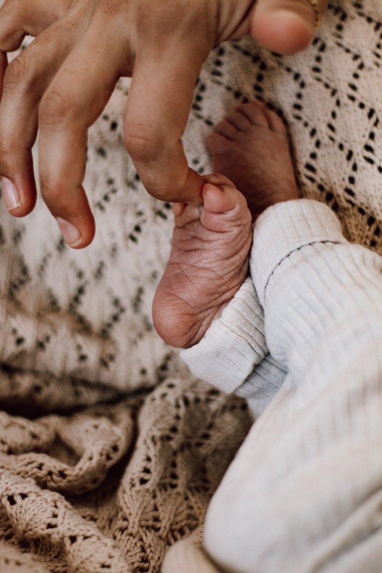 Mamas Finger kitzelt Fuß eines Neugeborenen